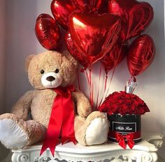 a teddy bear sitting on top of a table with red balloons and a box of roses