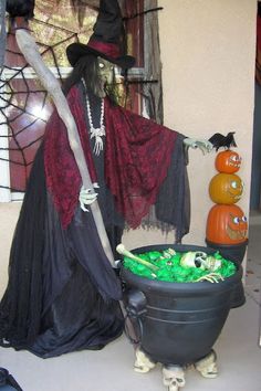 there is a halloween decoration in the house with pumpkins on the ground and a witch standing next to it