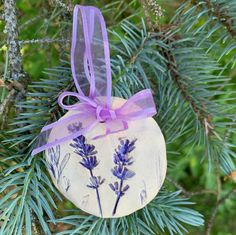 a ceramic ornament hanging from a tree with purple ribbon and lavender flowers on it