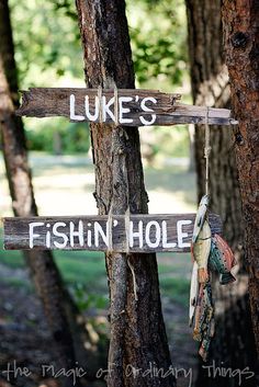 a wooden sign that says luke's fishin hole hanging from a tree in the woods