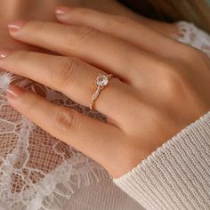 a woman's hand wearing a gold ring with a diamond on it and a white lace top