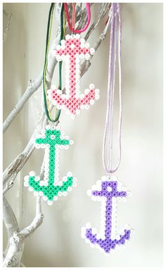 three beaded ornaments hang from a tree branch in the shape of an anchor and cross