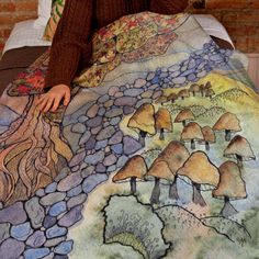 a woman sitting on top of a bed covered in a blanket with trees and rocks