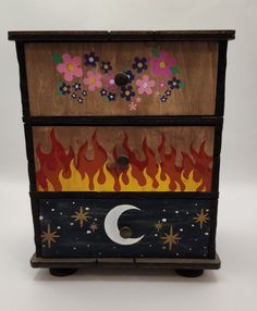 a wooden box with fire and flowers painted on the side, sitting in front of a white background