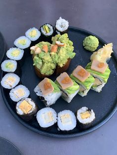 sushi and avocado are arranged on a black plate