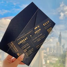 a person holding up a black and gold ticket in front of a cityscape