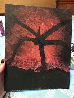 a person holding up a piece of art that looks like a cross on a red and black background