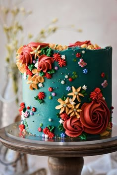 a blue cake with red and orange flowers on it sitting on top of a table