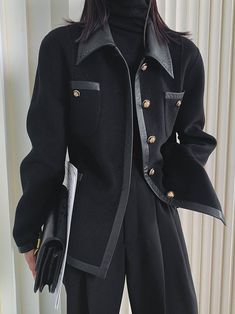 a woman wearing a black coat and hat standing in front of a white wall with her hands on her hips