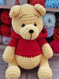 a crocheted teddy bear wearing a red sweater sits in front of skeins of yarn