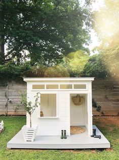 a small white shed sitting on top of a grass covered field next to a tree