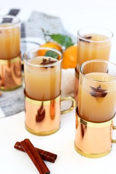 four glasses filled with liquid sitting on top of a table next to oranges and cinnamon sticks