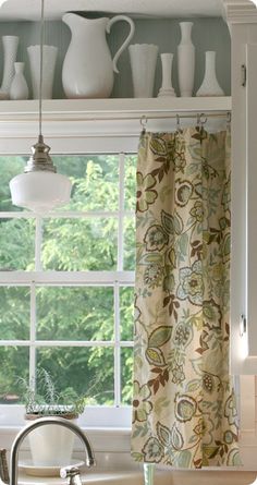 a kitchen window with curtains and a light hanging from it's side in front of the window