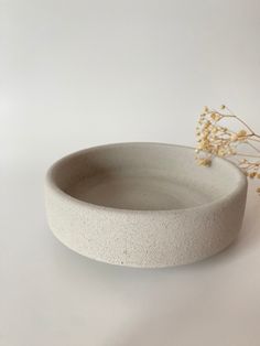 a white bowl sitting on top of a table next to a vase filled with flowers