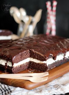 a chocolate cake with white frosting is cut into pieces and sits on a cutting board