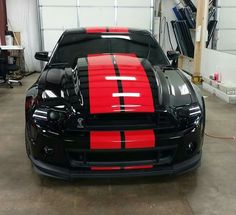 the front end of a black and red sports car in a garage with its hood up