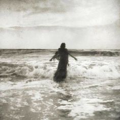 a woman standing in the ocean with her arms outstretched