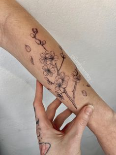 two hands holding each other with tattoos on their arms and arm, one has a flower tattoo on it