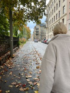 a woman walking down the street with an umbrella in her hand and autumn leaves on the ground