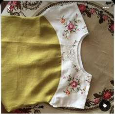 a yellow and white dress with flowers on it sitting on top of a floral table cloth