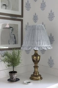 a lamp sitting on top of a white table next to a potted plant and framed pictures