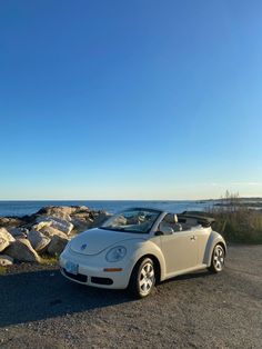 a white convertible car parked on the side of a road next to the ocean and rocks