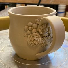 a white vase with flowers on it sitting on a table next to a cup that says pinelake pottery