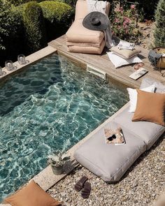 an outdoor pool with chaise lounges and pillows on the ground next to it