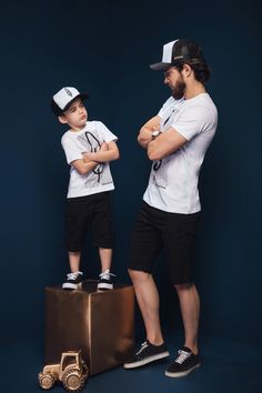 a man standing next to a little boy on top of a gold suitcase with his arms crossed