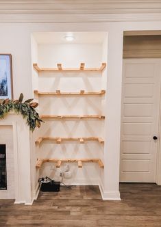 an empty living room with white walls and wood shelves on the fireplace mantels