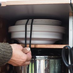 a person is holding a black handle near many plates and pans in a cabinet