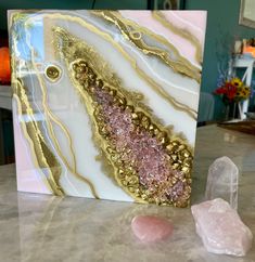 a pink and white marble with gold accents sits on a table next to some crystals