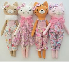 five stuffed animals are lined up in a row on a white surface, one is wearing a pink dress and the other has a flowered cat