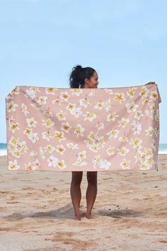 a woman standing on top of a sandy beach holding a pink flowered towel over her face