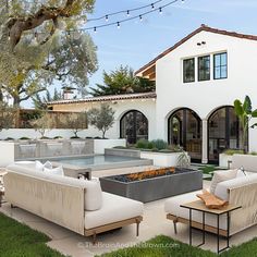 an outdoor living area with couches, tables and fire pit in front of a house