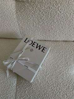 the book is laying on top of the white bedding and has a ribbon tied around it