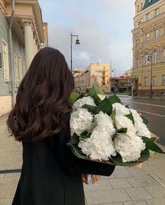 a woman walking down the street holding a bouquet of white flowers in front of her