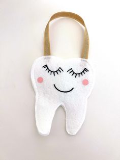 a tooth shaped bag with eyes and eyelashes hanging from it's front loop on a white background