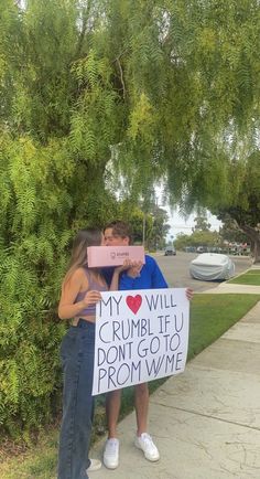 two people standing next to each other holding a sign that says my love will crumble u don't go to prom