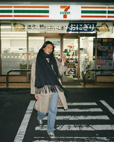 a woman walking across a cross walk in front of a convenience store with her hand up