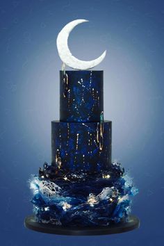 a three tiered blue and black cake with a crescent decoration on top, against a blue background