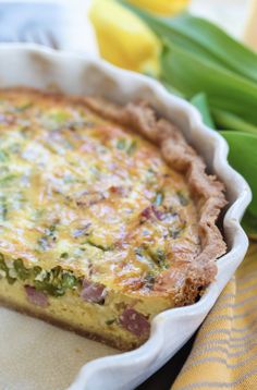 a quiche with ham and cheese in a pie pan next to green asparagus