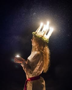 a woman wearing a crown with candles on her head and holding a lit candle in her hand