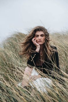 a woman sitting in tall grass with her hand on her chin and looking at the camera