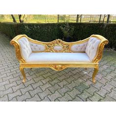 a gold and white couch sitting on top of a brick floor next to a hedge