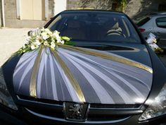 a black car with a silver and gold striped cover on it's hood is decorated with flowers