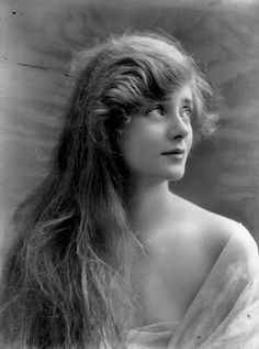 an old black and white photo of a woman with long hair in a dress looking off to the side