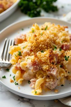 a white plate topped with macaroni and cheese covered in meat next to a fork