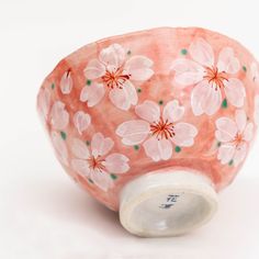 a pink vase with flowers painted on it's side, sitting on a white surface