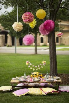 a picnic table with pink, yellow and white paper lanterns hanging from it's branches